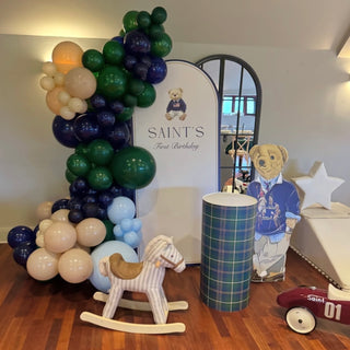 Teddy Bear Birthday Backdrop | Green and navy balloon display with bear cut-out, tartan cake plinth and rocking horse